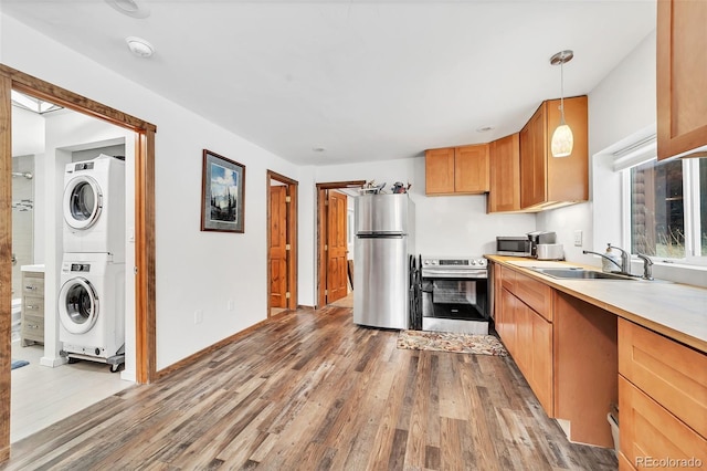 kitchen featuring stacked washing maching and dryer, sink, hanging light fixtures, stainless steel appliances, and light hardwood / wood-style flooring