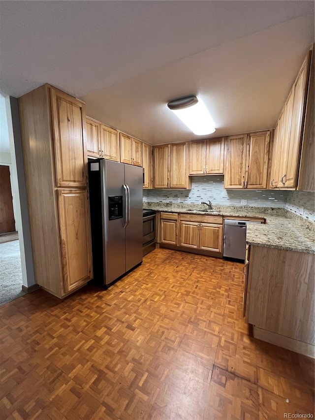 kitchen with light stone counters, sink, dark parquet floors, and stainless steel appliances