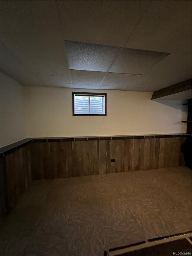 basement with a paneled ceiling, wooden walls, and carpet