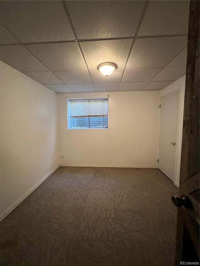 basement with a paneled ceiling and dark carpet