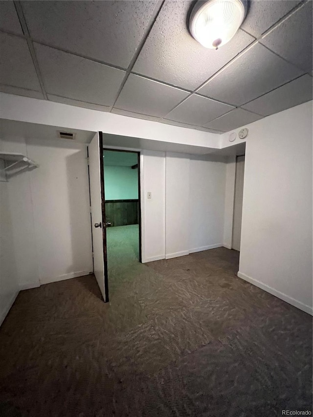 basement featuring a paneled ceiling and dark carpet