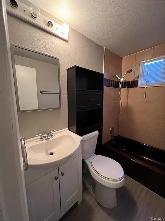 full bathroom featuring tiled shower / bath combo, hardwood / wood-style floors, a textured ceiling, toilet, and vanity