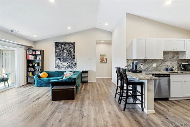 kitchen with dishwasher, a breakfast bar, lofted ceiling, light stone countertops, and white cabinetry