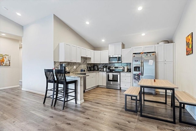 kitchen with white cabinets, light wood-type flooring, stainless steel appliances, and light stone counters