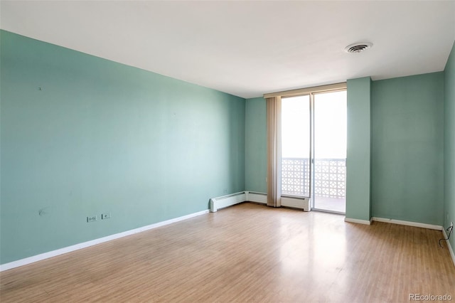 unfurnished room with a wall of windows, wood finished floors, visible vents, and baseboards