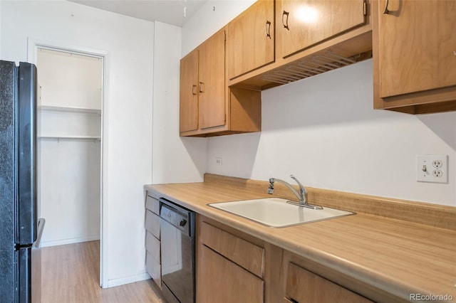 kitchen featuring light countertops, dishwasher, a sink, freestanding refrigerator, and light wood-style flooring