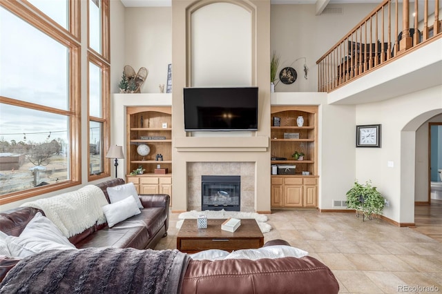 living room featuring plenty of natural light, a towering ceiling, a fireplace, and built in shelves