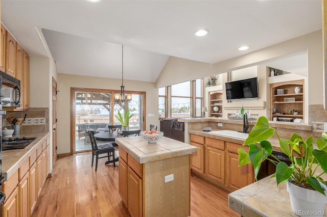 kitchen with lofted ceiling, sink, tile countertops, a center island, and light hardwood / wood-style flooring