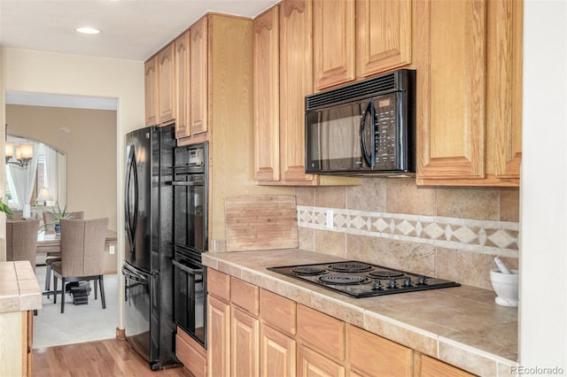 kitchen featuring decorative backsplash, tile counters, black appliances, light brown cabinets, and light wood-type flooring