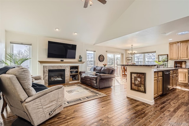 living room with dark wood-style floors, vaulted ceiling, ceiling fan with notable chandelier, and a high end fireplace