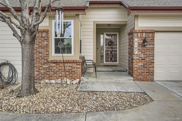 entrance to property with a garage, a shingled roof, and brick siding