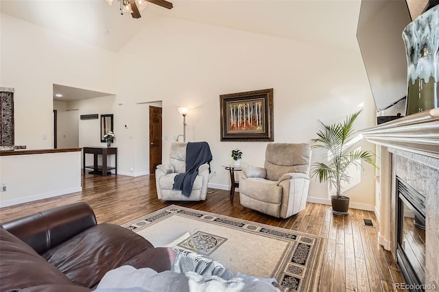 living area with hardwood / wood-style floors, a ceiling fan, high vaulted ceiling, a tile fireplace, and baseboards