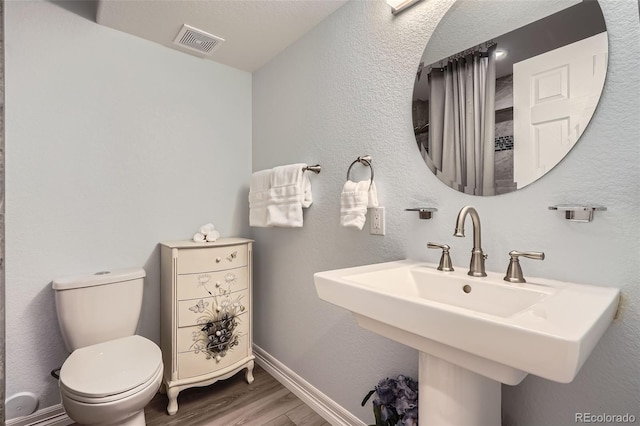 bathroom featuring visible vents, toilet, a sink, wood finished floors, and baseboards