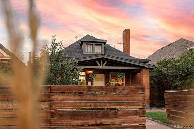 view of front of home with a shingled roof, brick siding, a porch, and a chimney