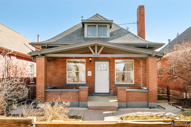 bungalow-style house featuring a shingled roof, brick siding, fence, and a chimney