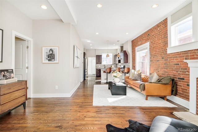 living room featuring recessed lighting, brick wall, a fireplace, baseboards, and dark wood finished floors