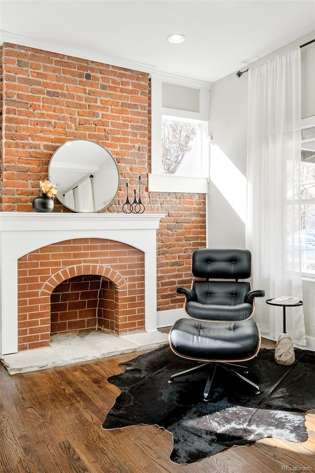 living area featuring a brick fireplace, brick wall, crown molding, and wood finished floors