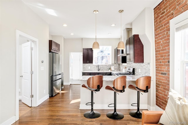 kitchen featuring dark brown cabinetry, light wood finished floors, gas range, freestanding refrigerator, and a peninsula