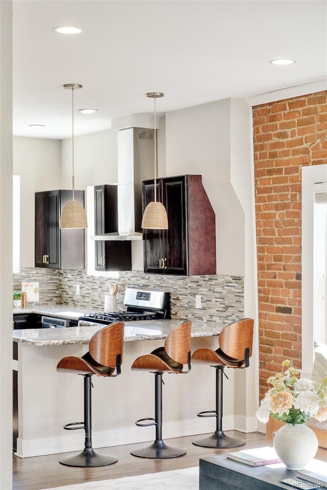 kitchen with stainless steel gas range, decorative backsplash, wall chimney range hood, and a breakfast bar area