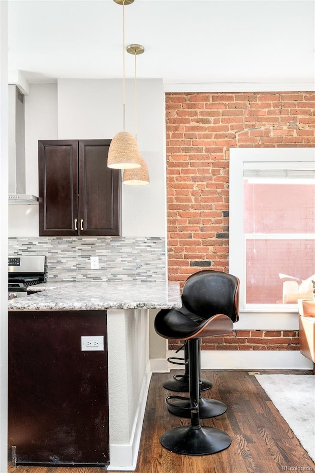 kitchen with decorative backsplash, dark wood finished floors, dark brown cabinets, wall chimney range hood, and stainless steel range with gas stovetop