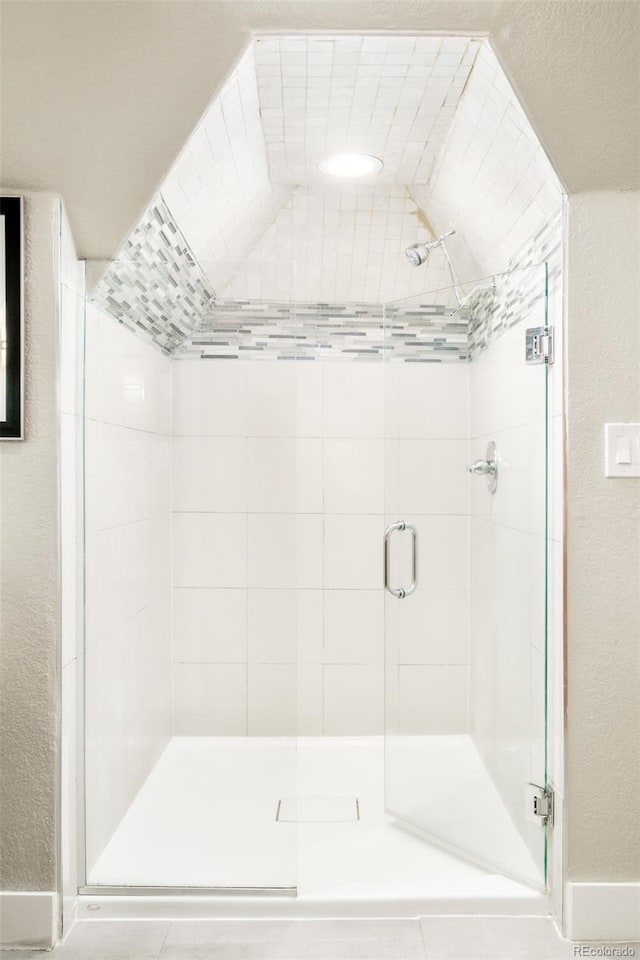 bathroom with a textured wall, a shower stall, and baseboards