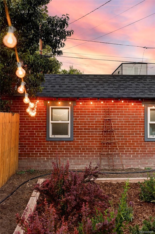 view of side of home with a shingled roof, brick siding, fence, and mansard roof