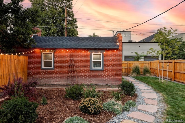 property exterior at dusk featuring brick siding, a fenced backyard, and roof with shingles