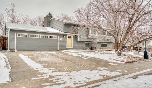 tri-level home featuring concrete driveway, a chimney, and an attached garage