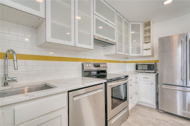 kitchen with a sink, white cabinetry, appliances with stainless steel finishes, light stone countertops, and glass insert cabinets