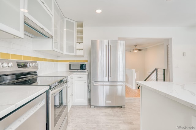 kitchen with white cabinetry, appliances with stainless steel finishes, backsplash, light stone countertops, and glass insert cabinets