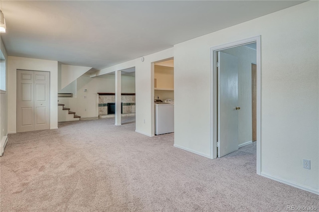 unfurnished room featuring a fireplace with raised hearth, stairway, light carpet, separate washer and dryer, and baseboards