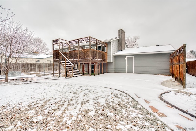 snow covered house with a chimney, fence, stairway, and a deck