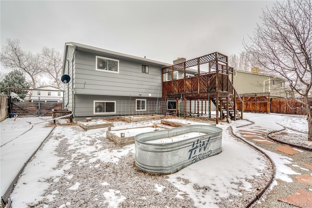 snow covered rear of property featuring a vegetable garden, fence, a wooden deck, and stairs