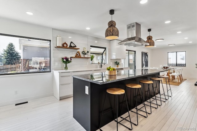 kitchen featuring a breakfast bar area, island range hood, white cabinetry, a center island, and modern cabinets