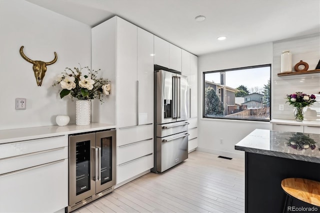 kitchen featuring beverage cooler, high end refrigerator, baseboards, light wood-style floors, and white cabinetry