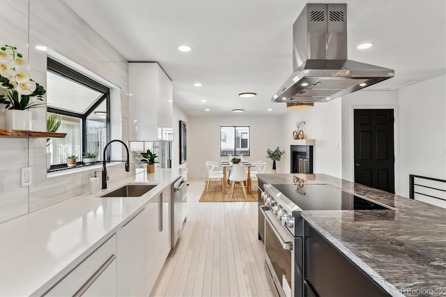 kitchen with white cabinets, modern cabinets, island exhaust hood, stainless steel stove, and a sink