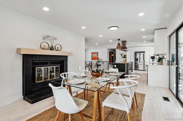 dining area with a brick fireplace, light wood-style flooring, visible vents, and recessed lighting