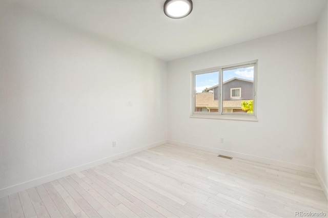 empty room with light wood-type flooring, visible vents, and baseboards