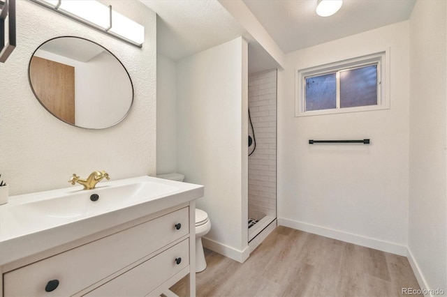 bathroom featuring toilet, a stall shower, vanity, wood finished floors, and baseboards