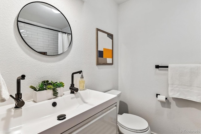 full bathroom with a textured wall, vanity, and toilet