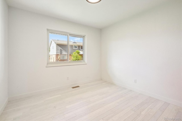 empty room with baseboards, visible vents, and light wood finished floors