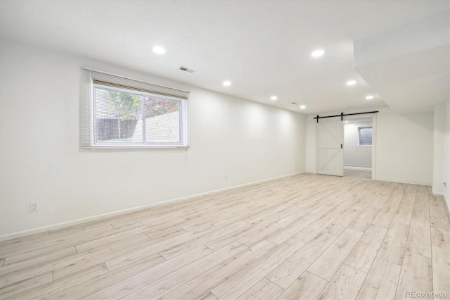 empty room featuring a barn door, visible vents, baseboards, light wood-style flooring, and recessed lighting