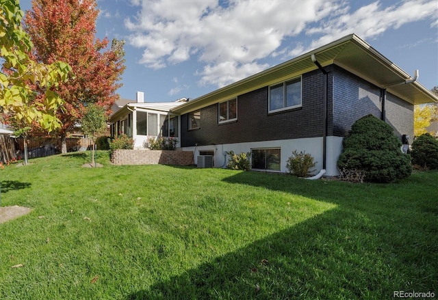 back of property with a yard, brick siding, a chimney, and fence