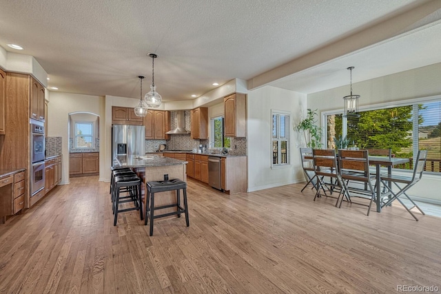 580 Eagle Nest Ct, Golden, CO 80401 - kitchen featuring wall chimney exhaust hood, appliances with stainless steel finishes, tasteful backsplash, a center island, and healthy amount of natural light
