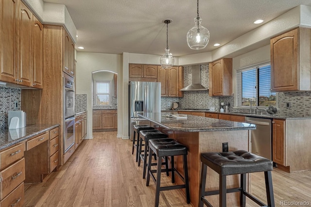 580 Eagle Nest Ct, Golden, CO 80401 - kitchen featuring wall chimney exhaust hood, a breakfast bar area, stainless steel appliances, decorative backsplash, and plenty of natural light