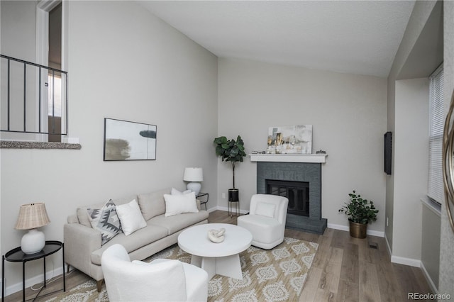 living room featuring hardwood / wood-style floors, lofted ceiling, a fireplace, and a textured ceiling