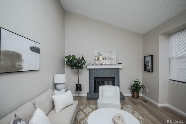 living room with wood-type flooring, vaulted ceiling, and a brick fireplace