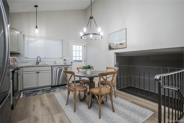 dining room with a notable chandelier, sink, high vaulted ceiling, and light hardwood / wood-style flooring