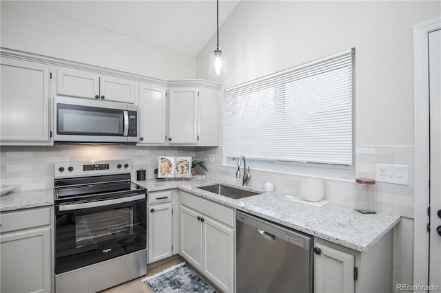 kitchen with lofted ceiling, white cabinets, sink, hanging light fixtures, and stainless steel appliances