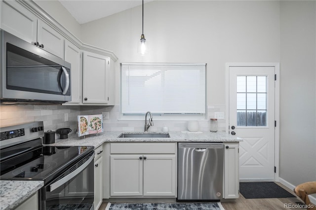 kitchen with hanging light fixtures, sink, appliances with stainless steel finishes, light stone counters, and white cabinetry